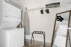 Closet with stacked washer and dryer, dresser, vacuum, full-length mirror and ironing board