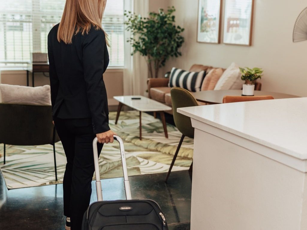 Woman walking into a furnished apartment with a suitcase