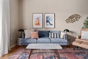 Furnished living room with blue sofa, marble coffee table, end tables, tables lamps and art