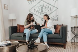 2 female Lodgeur guests on a sofa, chatting over coffee