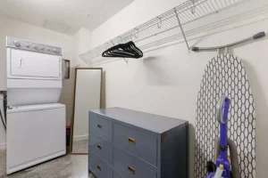 Closet with stacked washer and dryer, dresser, vacuum, full-length mirror and ironing board