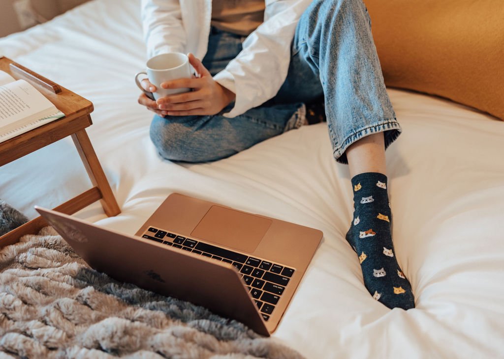 Woman on a bed with a laptop and coffee