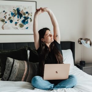 woman stretching on a bed with a laptop