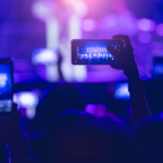 Person holding up cell phone at concert, capturing the excitement of live music.