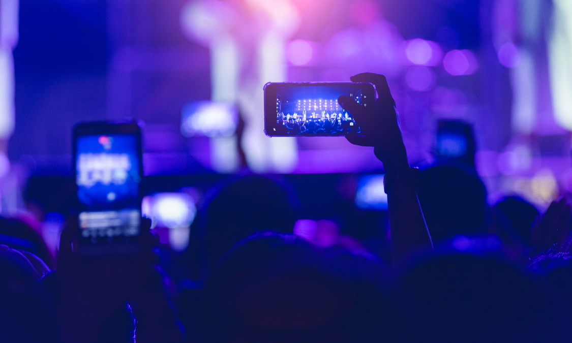 Person holding up cell phone at concert, capturing the excitement of live music.