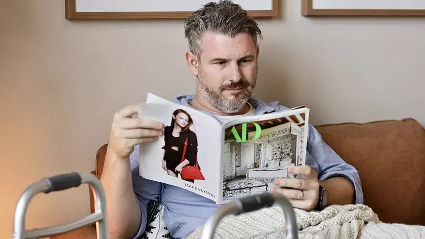 a man sitting on the couch reading with a walker next to him