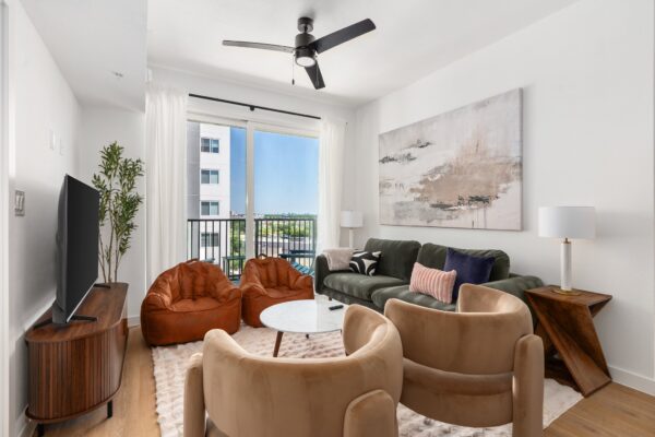 The living room of a three bedroom apartment in the Energy Corridor with a green sofa, sand-colored accent chairs, and bean bags in front a TV